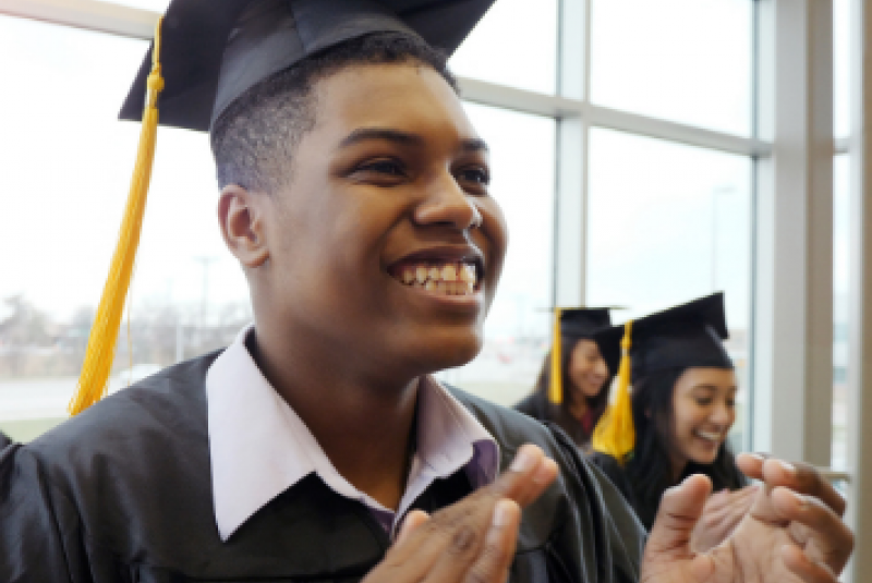 Young man clapping while wearing a cap and gown
